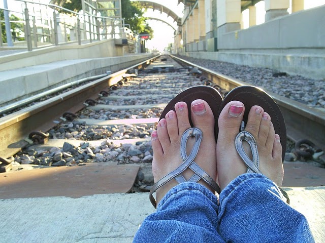 A picture of my feet in sandals, with the tracks in the background.